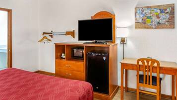 A hotel room with a bed, a desk, a television, and a refrigerator.