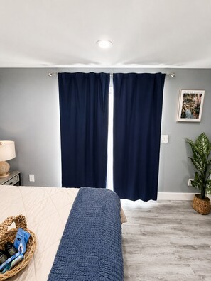 Un dormitorio con cama, mesita de noche, lámpara, un cuadro enmarcado en la pared y una planta en maceta.