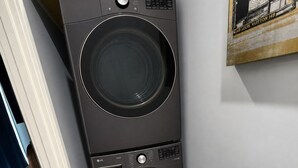 Eine schwarze LG THING Waschmaschine steht in einer Ecke eines Raumes mit einer weißen Tür und einem dunklen Holzschrank.