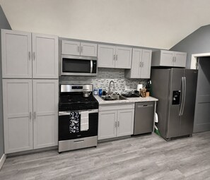 A modern kitchen with grey cabinets, a stainless steel refrigerator, a microwave, and a stove. - Brand-New, Lovely 2026 ADU - Near Major Hospitals, SoFi Stadium & LAX (Los Angeles)