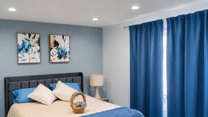 Ein Schlafzimmer mit einem Bett, einem Nachttisch, einer Lampe und einem Fenster mit Vorhängen.