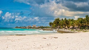 Uma praia com areia branca, ondas do oceano e palmeiras.