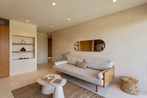 A modern living room with a sofa, coffee table, and a small round table with a book and a hat. - Luxury 3BR Condo at Aflora in Aldea Zama (Tulum)