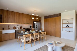 A modern kitchen with wooden cabinets, a central island, and a dining area with a round table and chairs. - Luxury 3BR Condo at Aflora in Aldea Zama (Tulum)