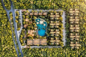 An aerial view of a resort with a central pool, multiple bungalow-style accommodations, and lush greenery surrounding the area. - Luxury 3BR Condo at Aflora in Aldea Zama (Tulum)