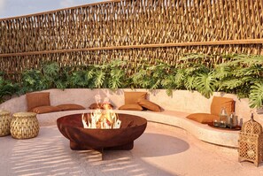 A fire pit surrounded by a seating area with cushions and a woven wall backdrop. - Luxury 3BR Condo at Aflora in Aldea Zama (Tulum)