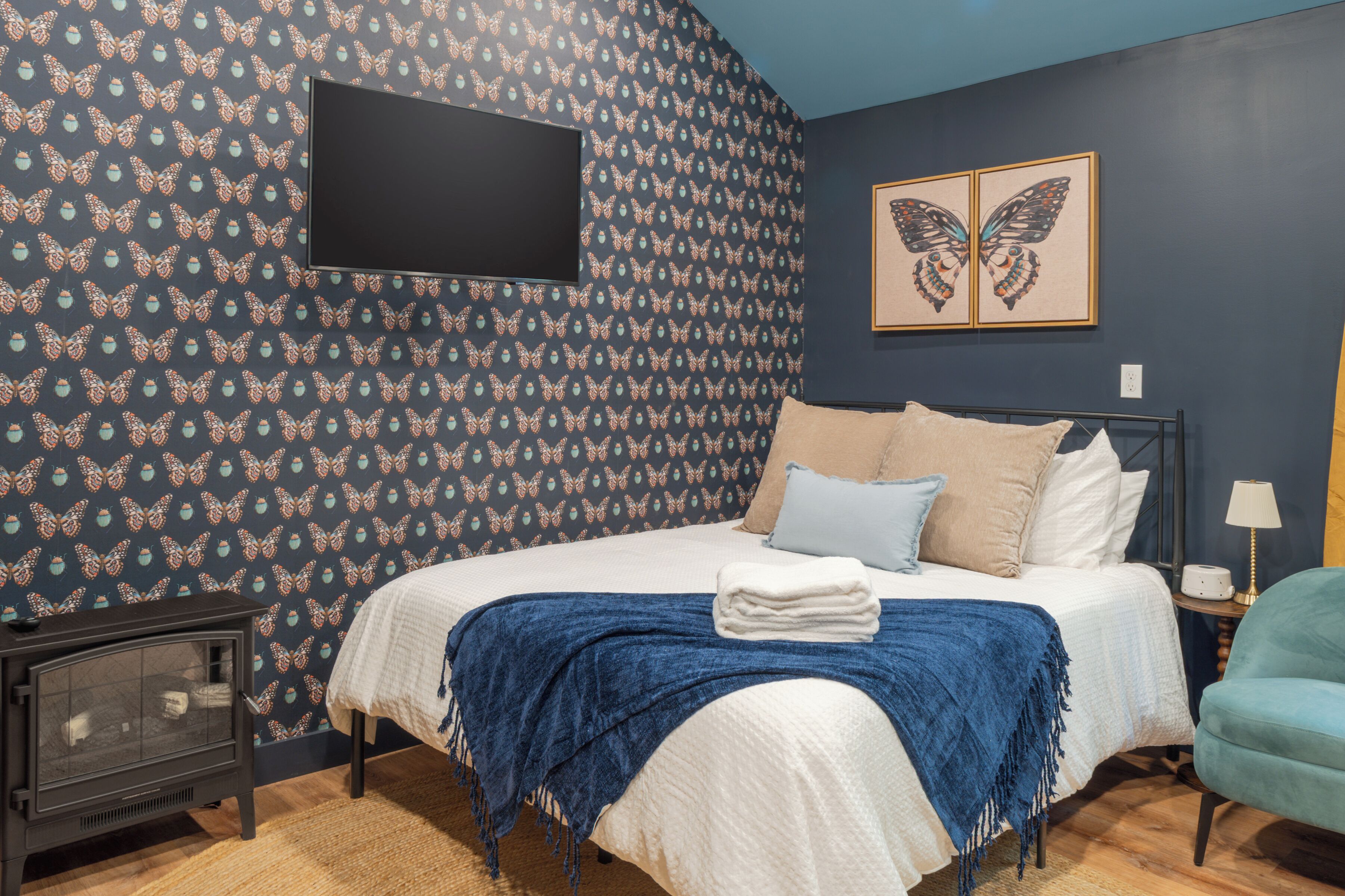 A bedroom with a bed, a flat-screen TV mounted on the wall, and a pair of butterfly artwork above the bed.