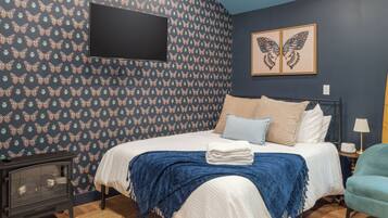 A bedroom with a bed, a flat-screen TV mounted on the wall, and a pair of butterfly artwork above the bed.