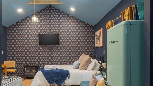 Une chambre à coucher comprenant un lit, une commode, une radio de style rétro et un téléviseur fixé au mur.
