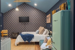 Un dormitorio con cama, cómoda, radio de estilo vintage y televisor montado en la pared.