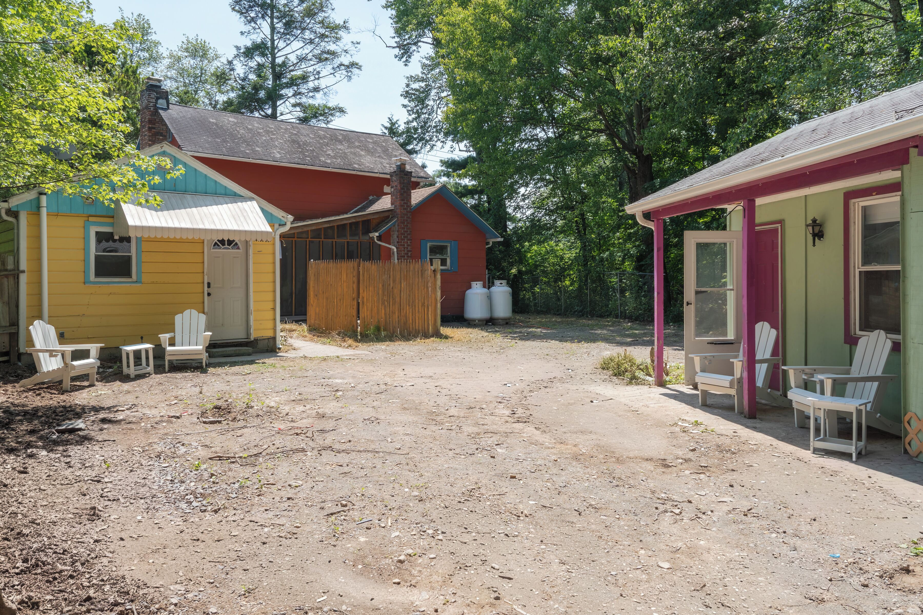 Une cabane rustique avec un sol en terre battue, une clôture en bois et deux petits abris contenant des chaises Adirondack.