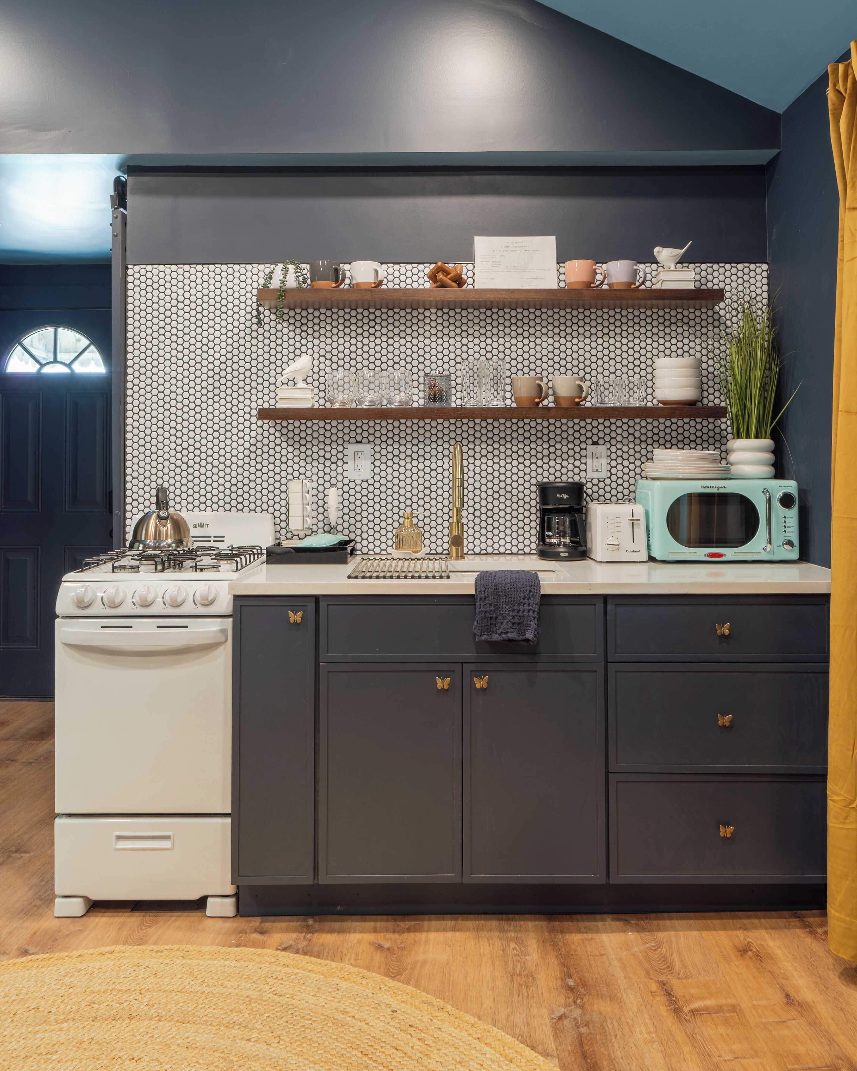 A kitchen with a stove, microwave, and shelves with kitchenware.