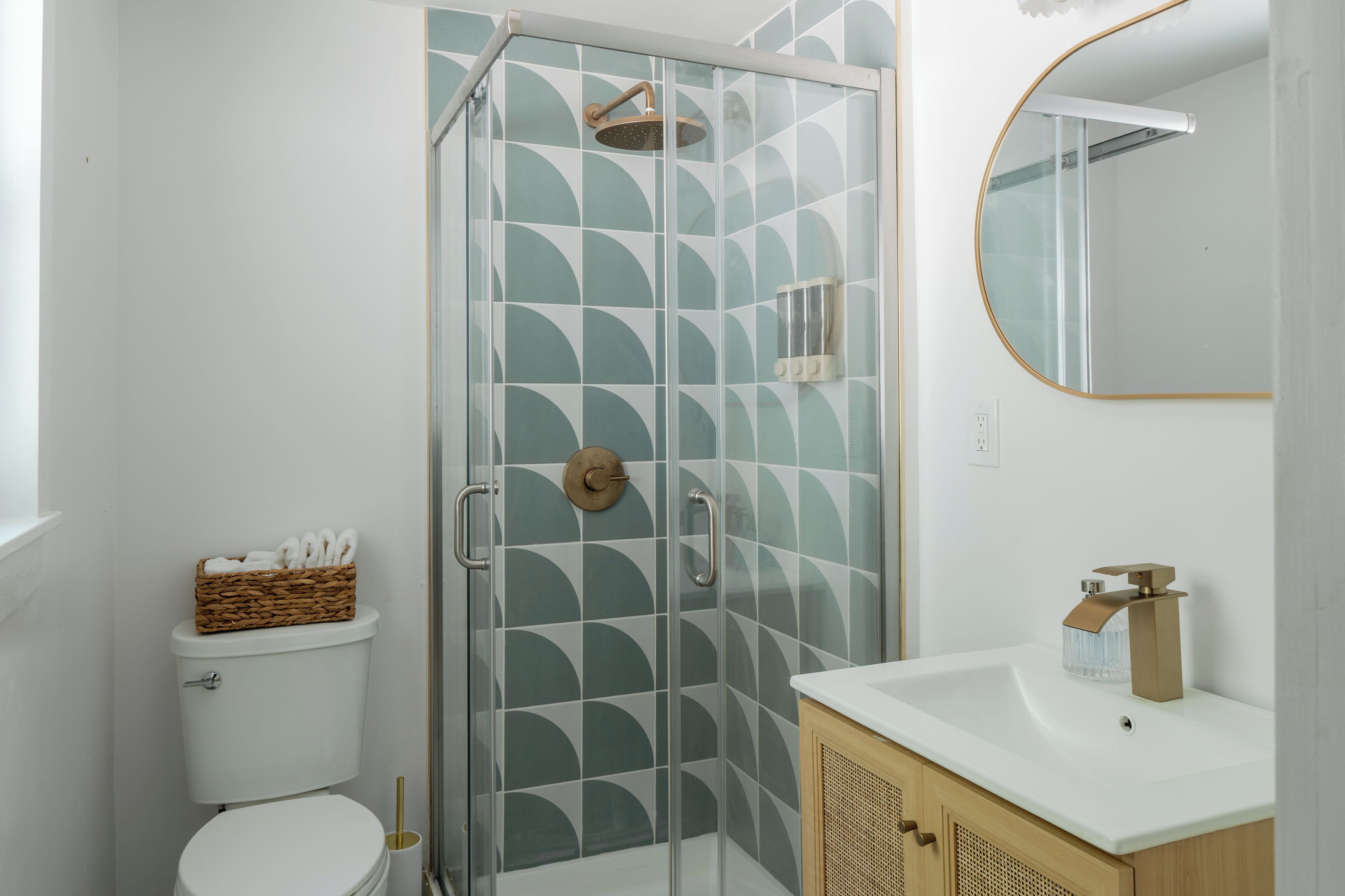 A bathroom with a glass shower enclosure, a toilet, and a sink with a mirror above it.