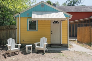 A small, single-story building with a yellow exterior and a blue roof. There are two white Adirondack chairs in front of the building.