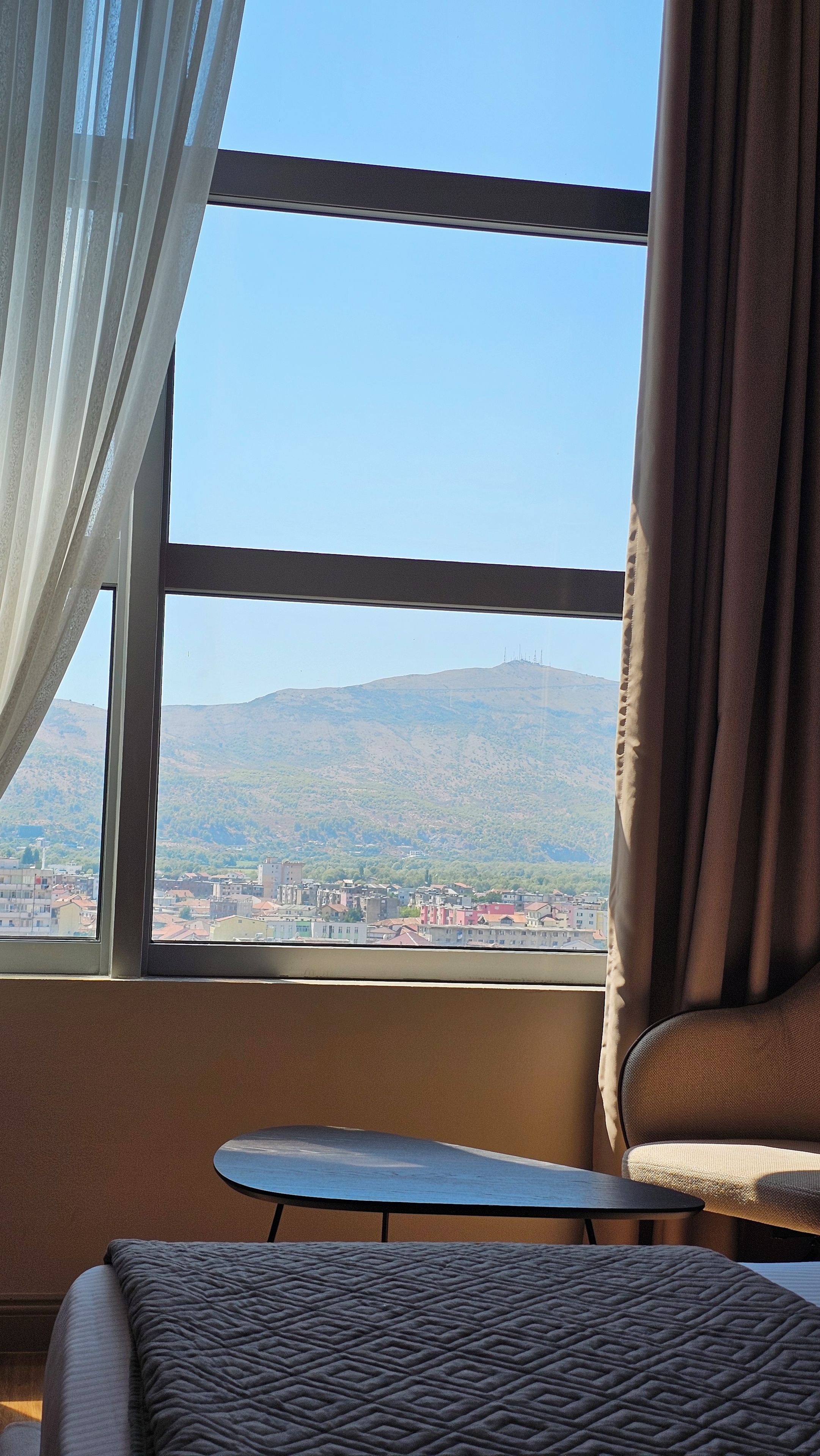 A room with a view of a cityscape and mountains through a large window.