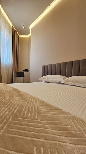 A hotel room with a bed, a headboard, a nightstand, and a desk with a coffee maker. - The Center 102 (Shkodër)