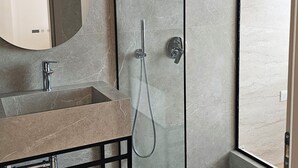 A modern bathroom with a glass-enclosed shower, a sink with a marble countertop, and a large mirror. - The Center 102 (Shkodër)