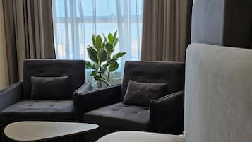 A hotel room with a bed, two armchairs, a small table, and a potted plant.