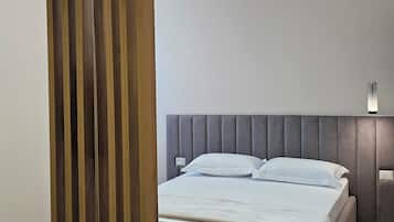 A modern bedroom with a grey upholstered headboard, a bed with white bedding, a wooden slatted partition, and a hanging pendant light.
