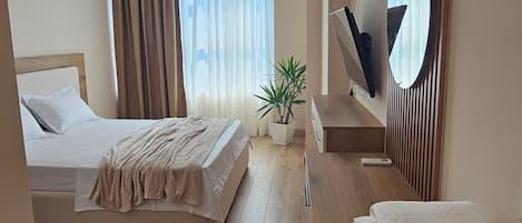 Habitación de hotel con cama, mesita de noche, espejo y una planta en maceta.