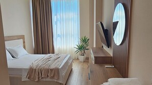 A hotel room with a bed, bedside table, mirror, and a potted plant. - The Center 102 (Shkodër)