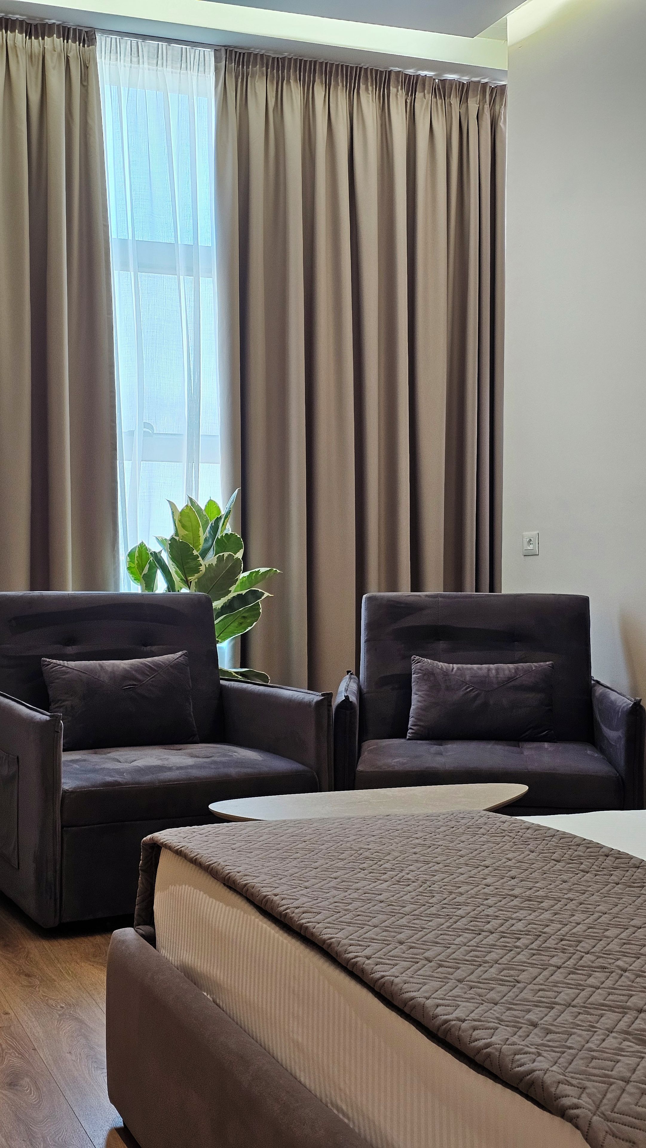 Una habitación con dos sofás, una cama y un amplio ventanal con cortinas.