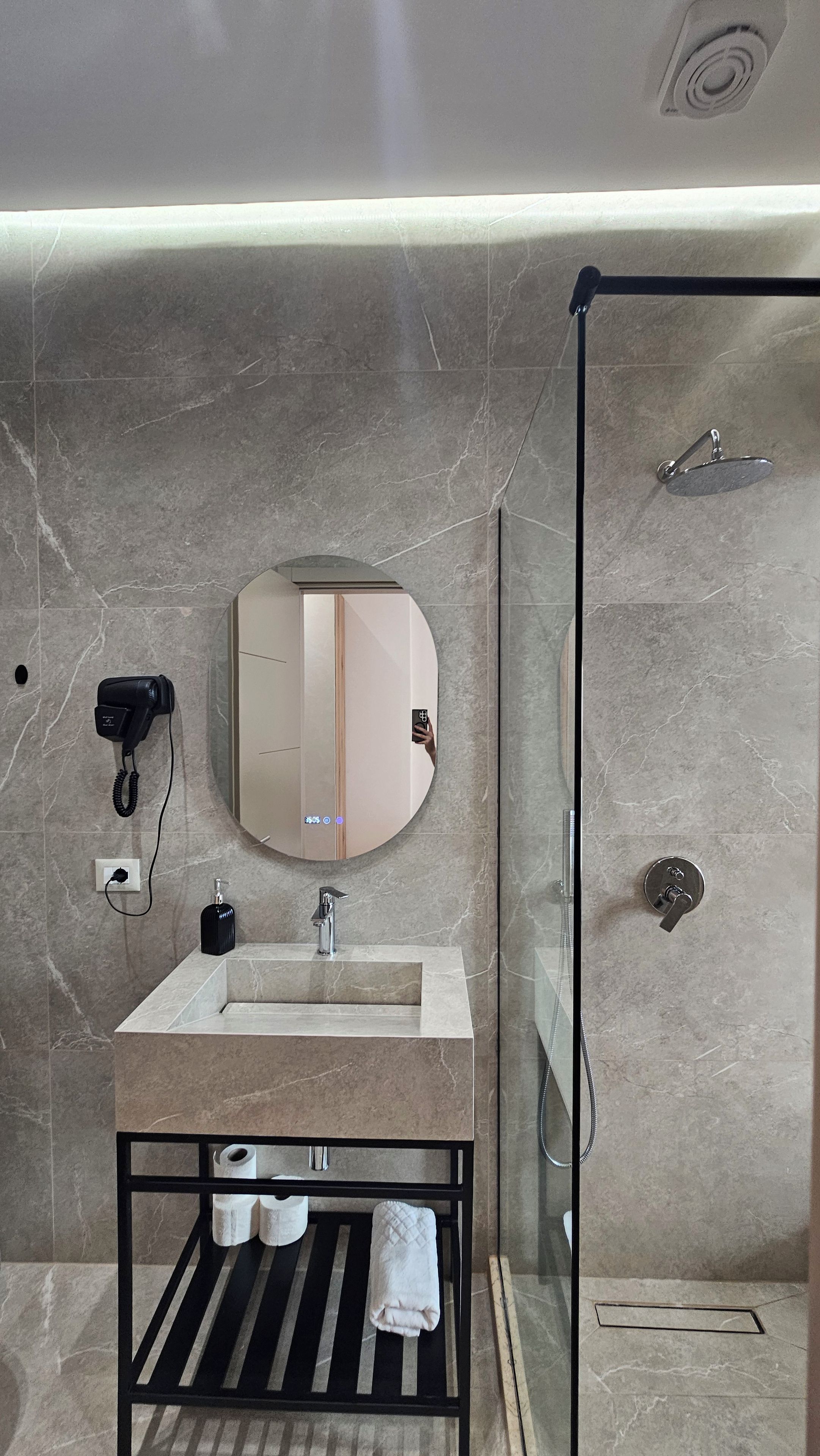 A modern bathroom with a marble sink, a handheld hair dryer, a glass-enclosed shower, and a towel rack.