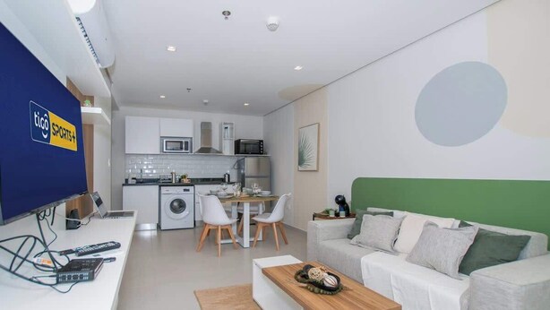 Een moderne woonkamer met een bank, een salontafel, een televisie en een keukenhoek met een eettafel en stoelen.