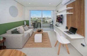 A modern living room with a sofa, a coffee table, a dining table, and a workspace with a laptop. - Corporate Stays First Living - 704 (Asunción)