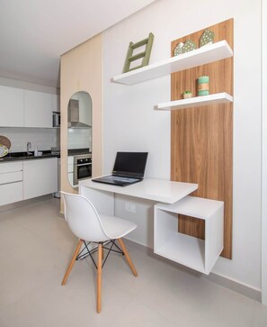 A modern kitchen with a built-in desk, a laptop, a white chair, and wooden shelves. - Corporate Stays First Living - 704 (Asunción)