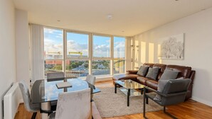 A modern living room with a glass dining table, leather sofa, and large windows offering a city view. - Skyline & Sea (Belfast)