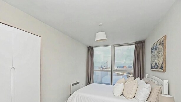 A bedroom with a large bed, a wardrobe, a window with curtains, and a city view. - Skyline & Sea (Belfast)