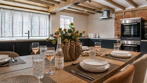 A dining area with a wooden table set for a meal, a vase with flowers, and a bottle of wine. - The Old Bakery - sleeps 6 guests in 3 bedrooms (Alderminster)