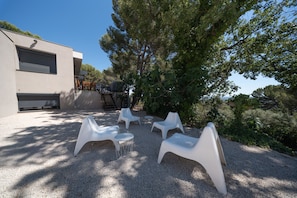 A building with a garage, outdoor seating area with plastic chairs, and a gravel ground. - Ground floor of a house in the countryside, (Éguilles)