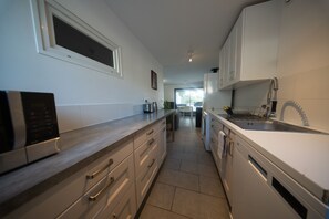 A modern kitchen with stainless steel appliances, white cabinetry, and a view into the dining area. - Ground floor of a house in the countryside, (Éguilles)