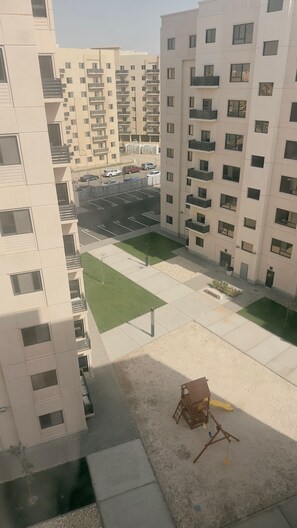 A multi-story residential building with balconies, a parking area, and a small playground.