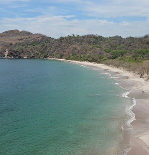 Eine Küstenlandschaft mit klarem türkisblauem Wasser, Sandstrand und spärlicher Vegetation an den Hügeln.