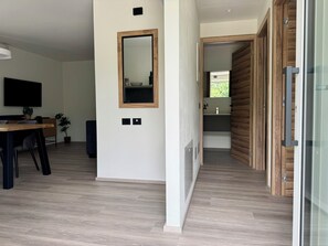 A modern interior with a dining area, a large mirror, and a hallway leading to a bathroom. - Apartment 8 – Palermo (Tremosine sul Garda)