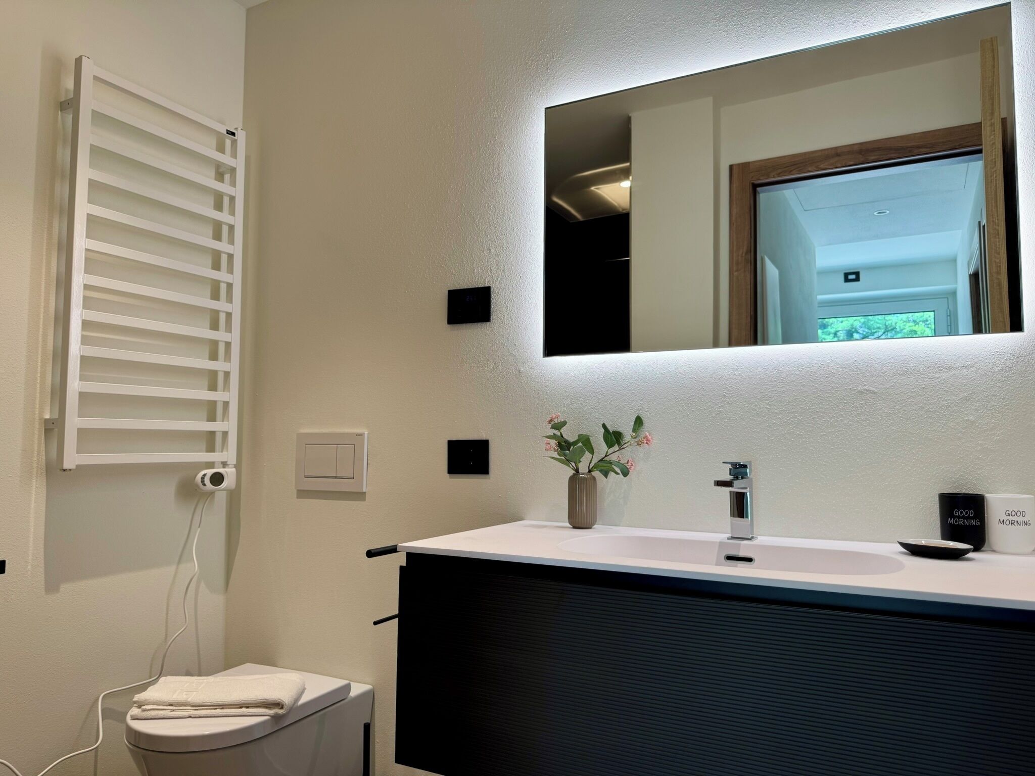 Ein Badezimmer mit einem weißen Waschtisch, einem Spiegel, einem Handtuchhalter, einer Toilette und einer kleinen Pflanze.