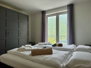 A hotel room with two beds, a wardrobe, and a balcony with a view of greenery. - Apartment 8 – Palermo (Tremosine sul Garda)