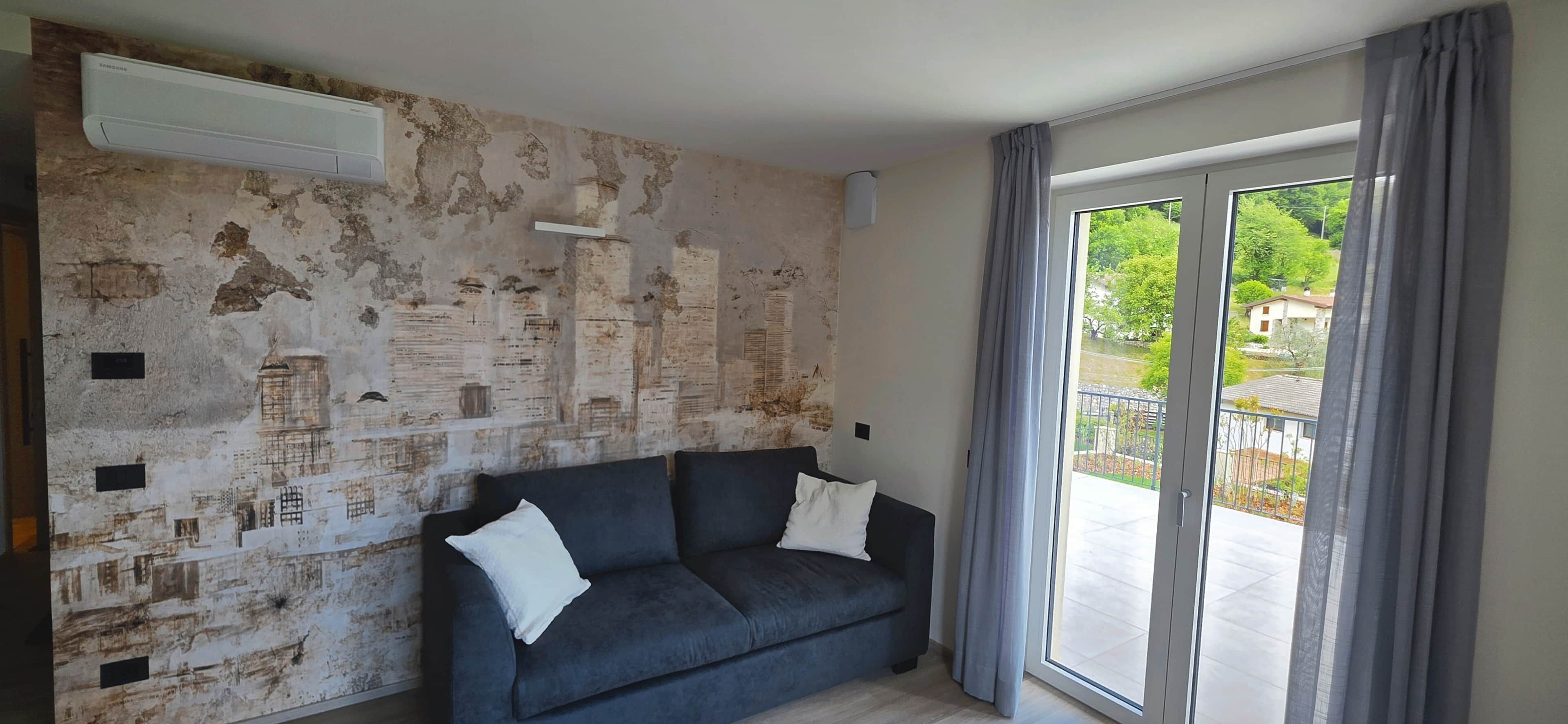 A room with a dark-colored sofa, a large window with curtains, and a wall with a distressed texture.