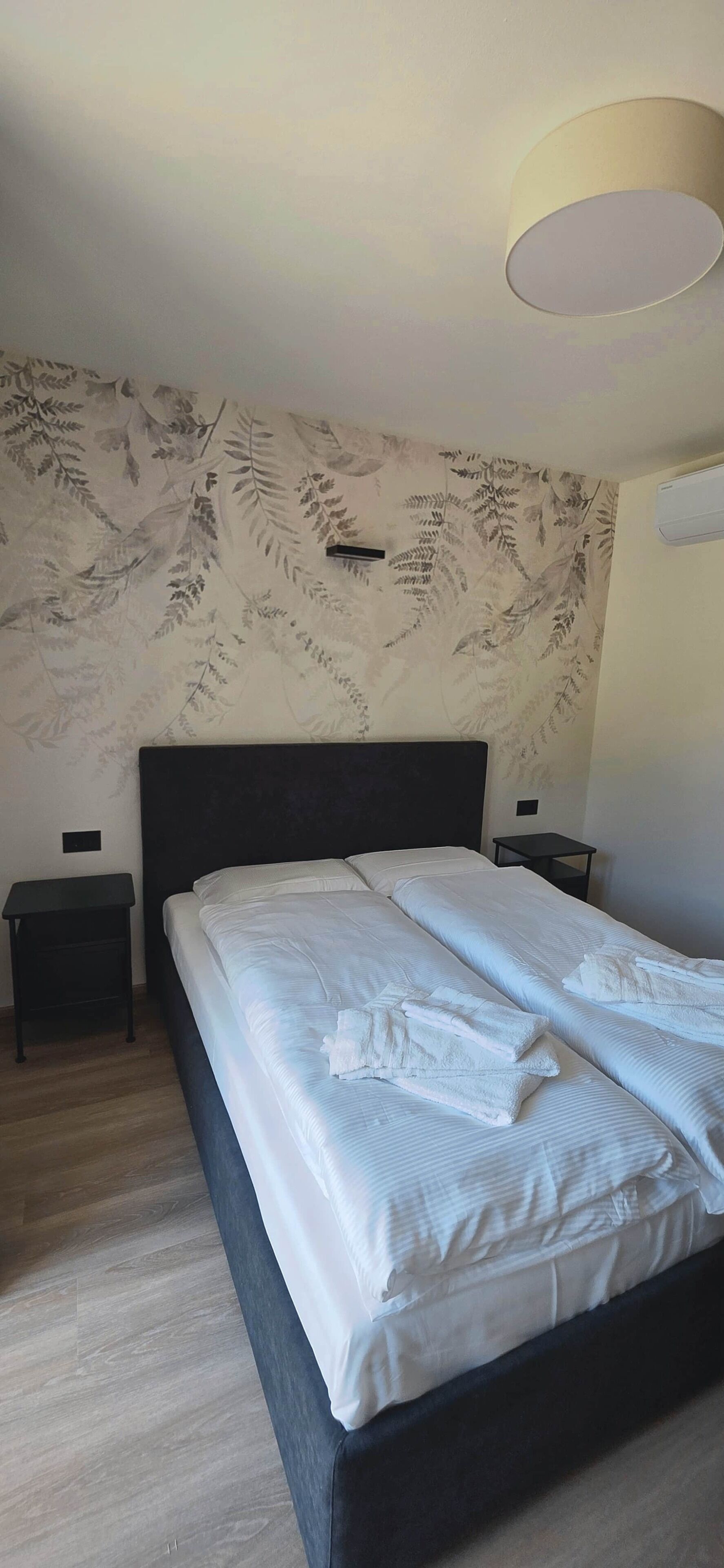 Une chambre à coucher avec un lit, deux tables de chevet, une lampe fixée au mur et un papier peint à motifs.