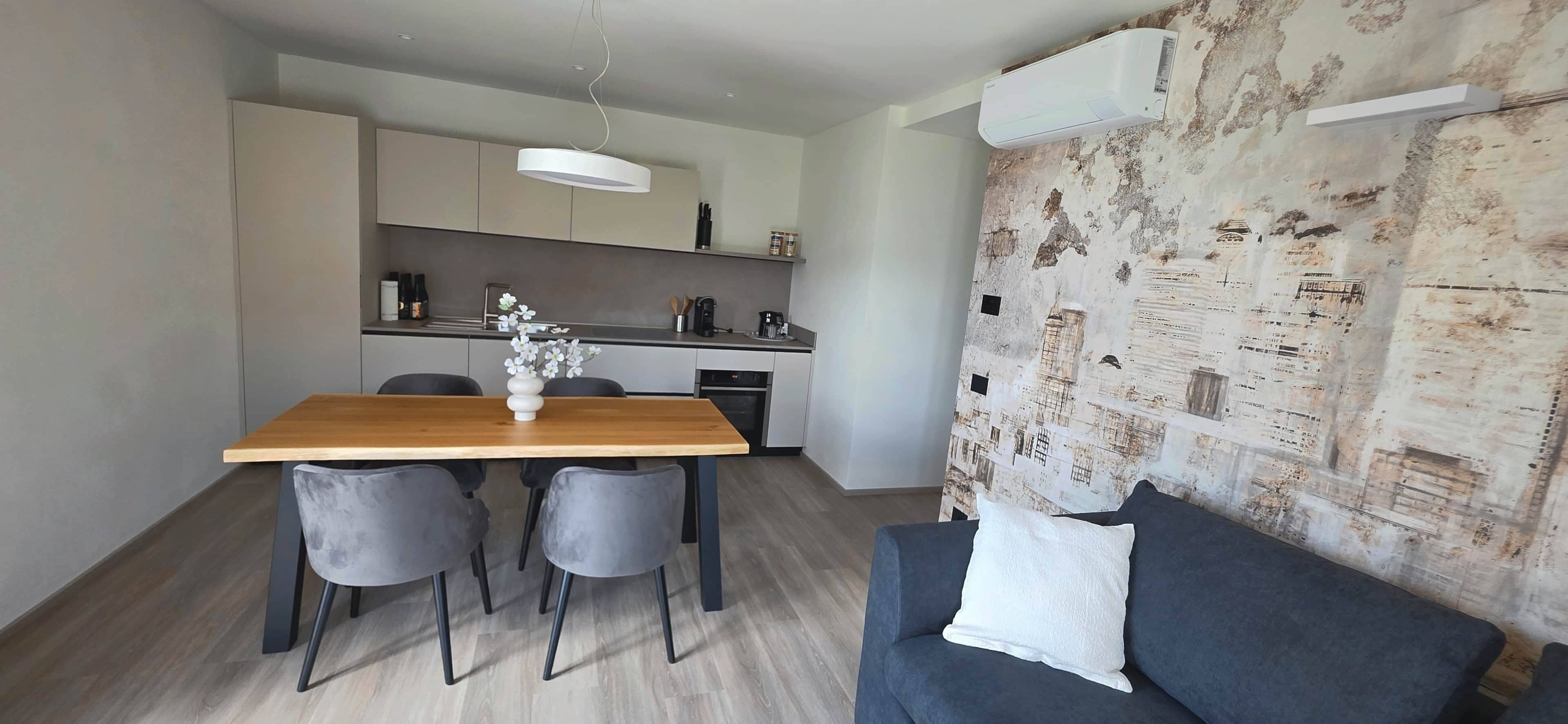 A modern kitchen with a dining table and chairs, a sofa, and a decorative wall.