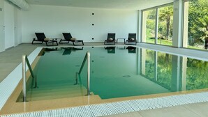 Ein Innenpool mit vier Liegestühlen, freiem Blick ins Freie und gefliestem Boden.