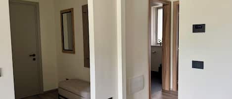 A room with a bed, a door, a mirror, and a thermostat on the wall.