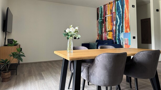 Ein moderner Essbereich mit einem Holztisch, grauen Polsterstühlen und einer Vase mit Blumen.