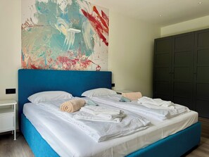 Une chambre moderne avec un grand lit, du linge de lit blanc et une tête de lit bleue.