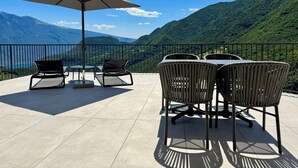Una terraza al aire libre con una mesa, sillas, un amplio paraguas y vistas panorámicas a la montaña.