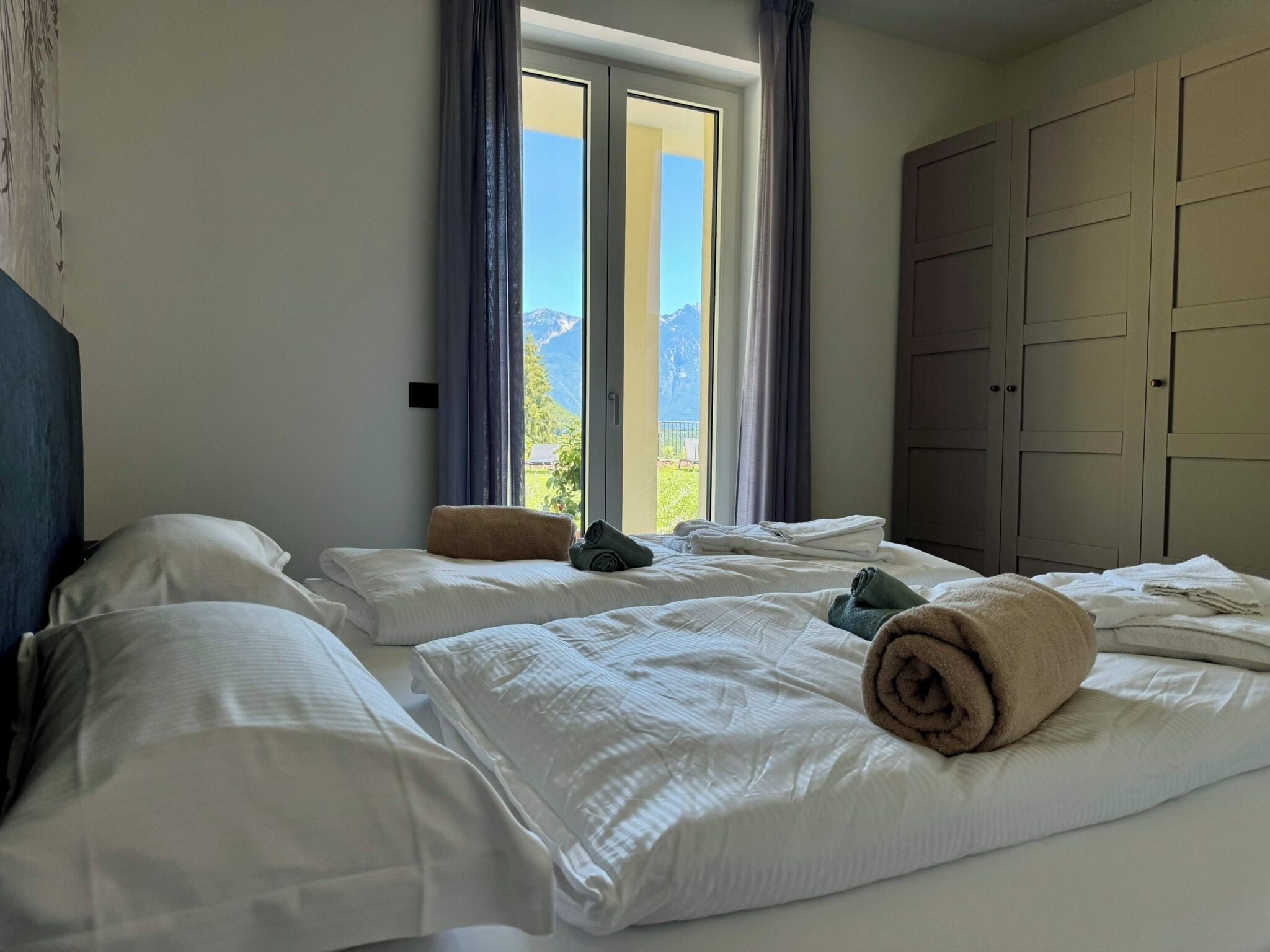 Ein Hotelzimmer mit zwei Betten, einem großen Fenster mit Vorhängen und einem Kleiderschrank.