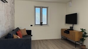 Una sala de estar con un sofá gris oscuro, un mueble de madera y un televisor montado en la pared.